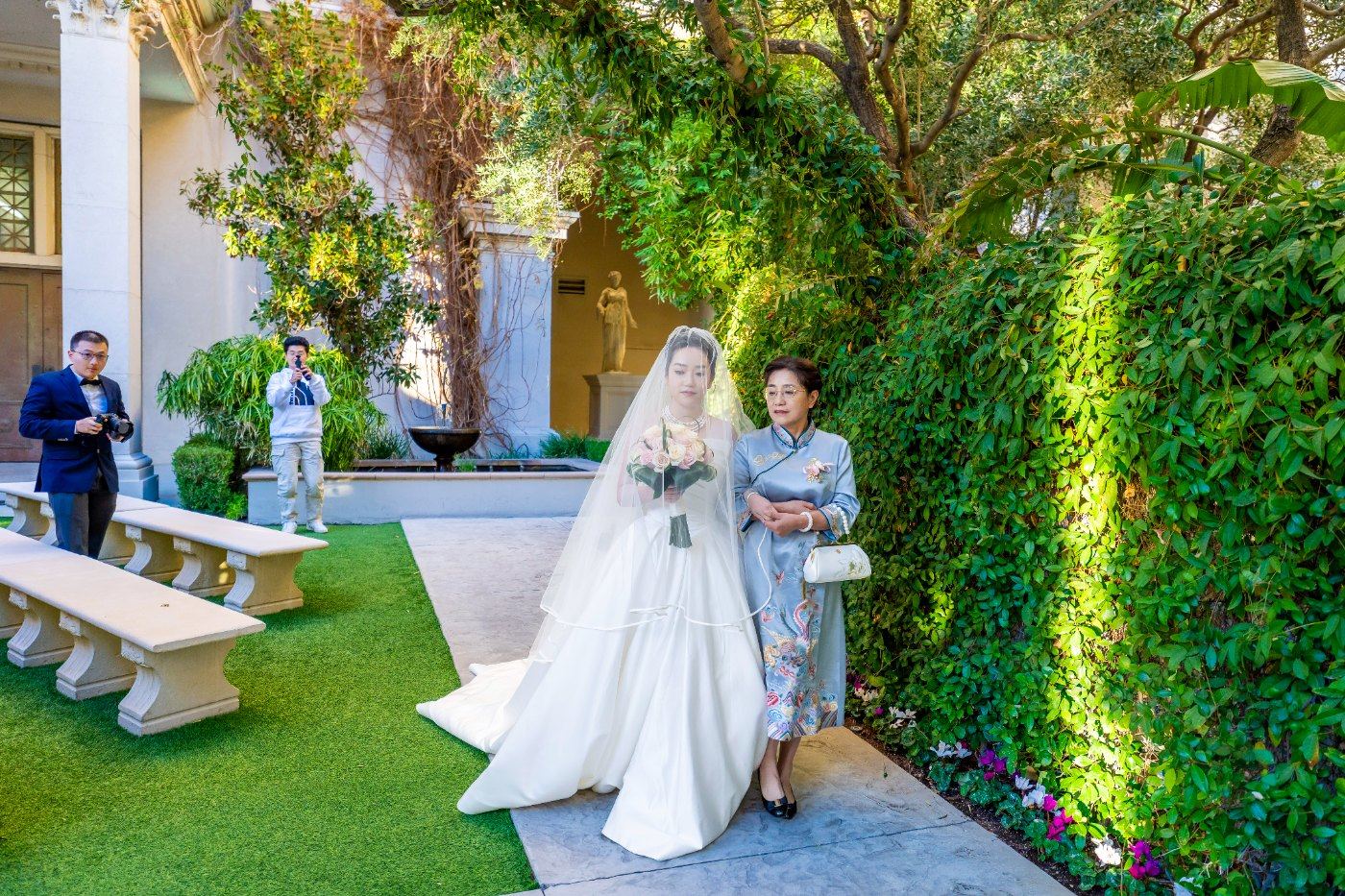 Las Vegas wedding photography — the bride walking in with her mother past a wall of greenery